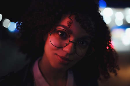 Portrait of young cute curly afro american girl. Night city lights. Neon illuminationの写真素材