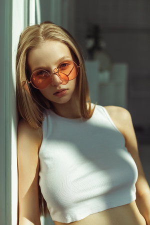 Young blonde girl with pink sunglasses. Indoor portrait with soft sunlight. Pretty baby face modelの写真素材