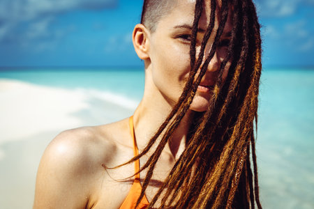 Beautiful dreadlocks woman relaxing on the beach. Brunette tanned girl in swimwear enjoying vacationの写真素材