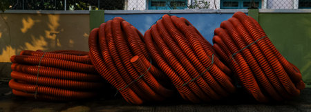 Stack of large red plastic hoses coiled against colorful wall outdoors.