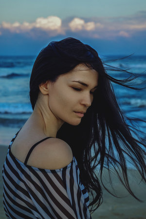 Serene ocean breeze with woman in striped shawl, peaceful coastal evening scene