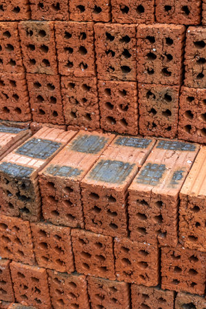 Stack of red clay bricks in construction site with textured surface.