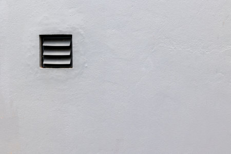 Gray wall with small ventilation grate on minimalist surface.