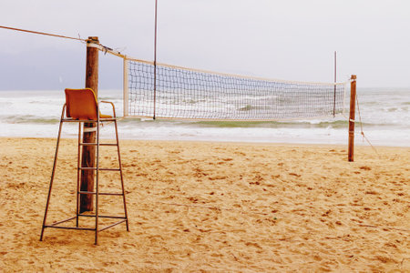 Empty beach volleyball court with chair overlooking ocean waves on cloudy day.の写真素材