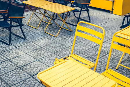 Outdoor cafe setting with yellow chairs and tables on patterned pavement.の写真素材