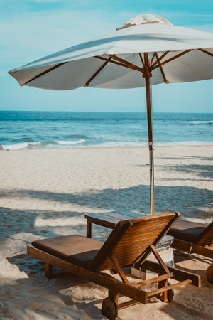 Serene beach scene with wooden lounge chairs and umbrella by the ocean.の写真素材