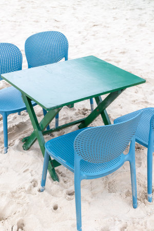 Green table and blue chairs on sandy beach.の写真素材