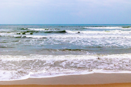 Tranquil beach scene with waves crashing on shoreline under clear sky.