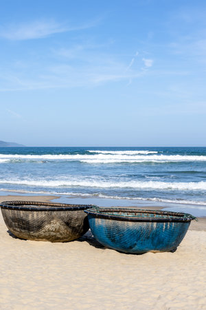 Traditional round fishing boats on sandy beach with gentle waves and clear blue sky.の写真素材