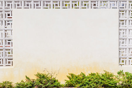 White concrete wall with decorative blocks and green shrubs below.の写真素材