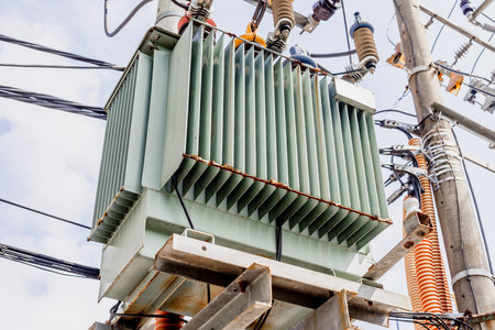 Electric power transformer on utility pole with wires and insulators against blue sky.
