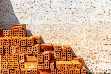 Stacked red bricks against weathered wall in sunlight.の写真素材