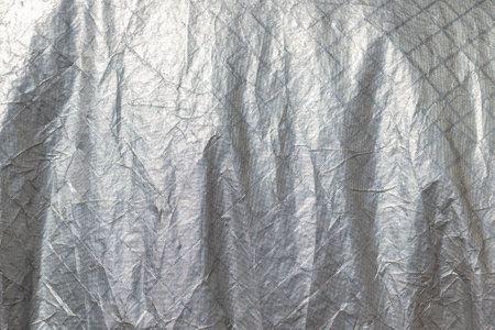 Wrinkled metallic silver fabric texture with geometric patterns.