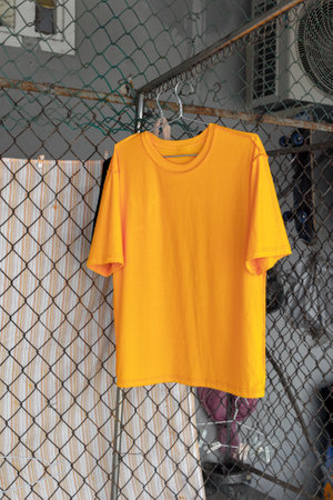 Bright orange t-shirt hanging on wire fence in urban setting.の写真素材