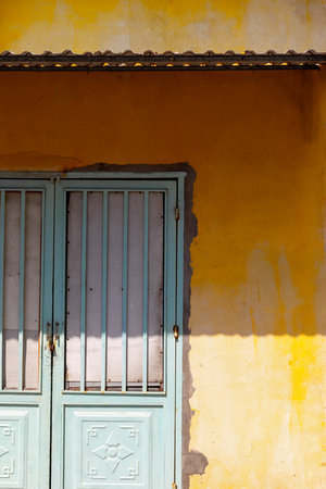 Blue metal door on yellow wall with sunlight shadows.の写真素材