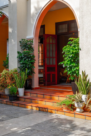 Charming entrance with red door and vibrant greenery on sunny day.の写真素材