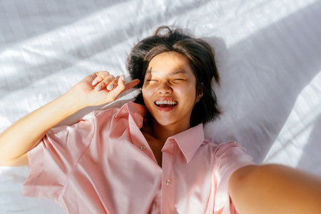 Asian female young adult smiling in pink shirt on white bed.