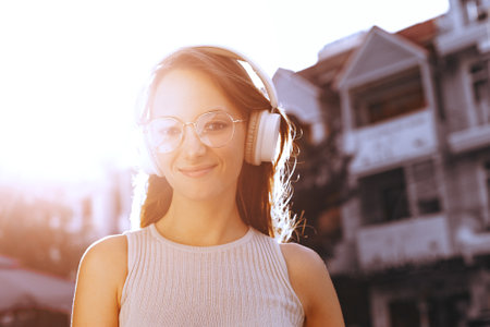 Young caucasian woman enjoying music with headphones outdoors in bright sunlight.