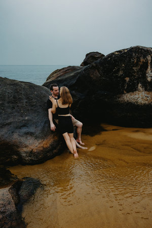 Young caucasian couple relaxing on sandy beach with large boulders.の写真素材