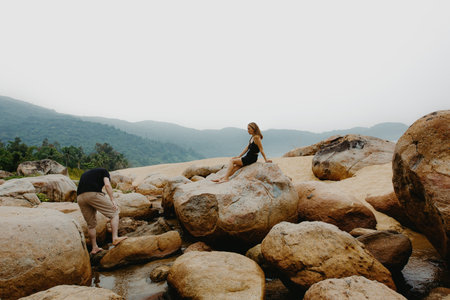 Young caucasian female relaxing on rocks in mountainous landscape, male exploring stream.の写真素材