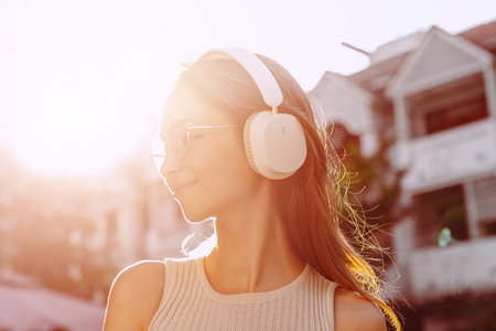 Young caucasian female enjoying music with headphones in sunlit urban setting.の写真素材