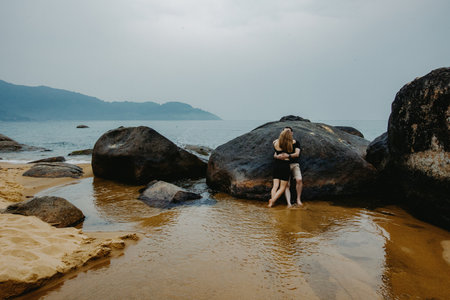 Young couple embracing on rocky beach under overcast sky.の写真素材