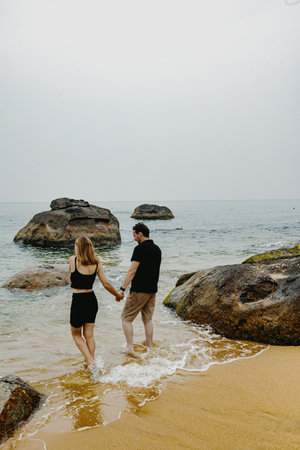 Young caucasian couple walking hand in hand on a rocky beach.の写真素材