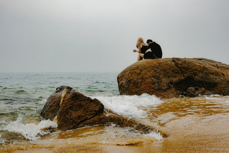 Young caucasian couple by the ocean on a rocky shoreline under a cloudy sky.の写真素材
