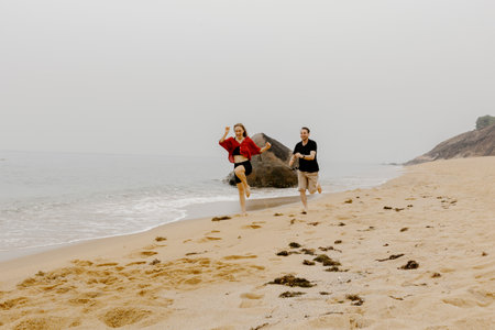 Young caucasian couple running and laughing on sandy beach.の写真素材