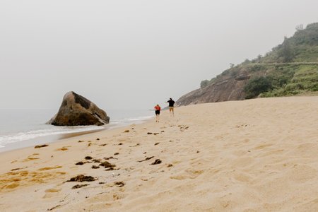 Couple enjoying a misty beach walk with rocks and cliffs in the background.の写真素材
