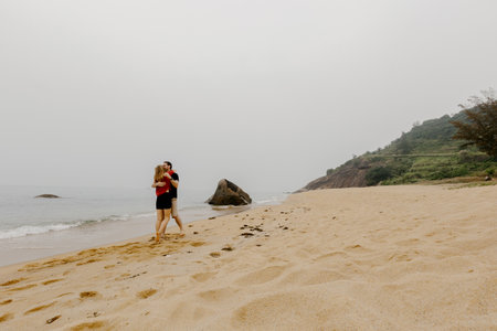 Couple embracing on sandy beach with scenic ocean view.の写真素材
