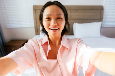 Young Asian female smiling in bedroom with pink shirt and short hair.の写真素材
