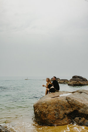 Caucasian couple relaxing on beach rock by calm ocean horizon.の写真素材