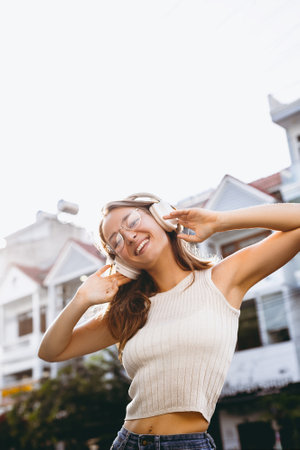 Young asian female enjoying music outdoors with headphones in casual summer outfit.の写真素材