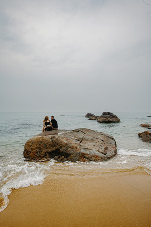 Female and male adults relaxing on rocky beachfront with ocean view.の写真素材