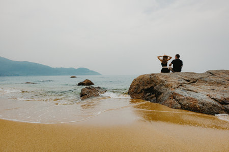 Caucasian adults sitting on beach rocks overlooking the ocean.の写真素材