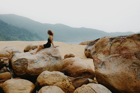 Young female relaxing on rocky beach with mountain view.の写真素材