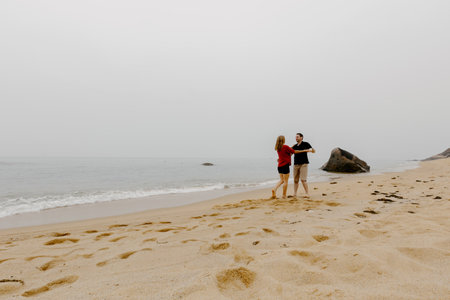 Couple enjoying a beach walk: young caucasian male and female embracing on sandy shore.の写真素材