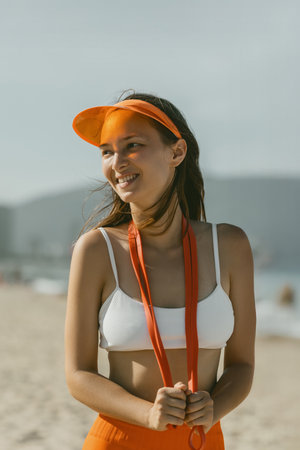 Young Asian woman enjoying a sunny beach day with orange visor and jump rope.の写真素材