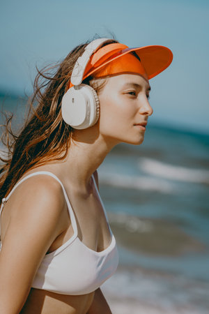 Young caucasian female enjoying beach with headphones and orange cap.の写真素材