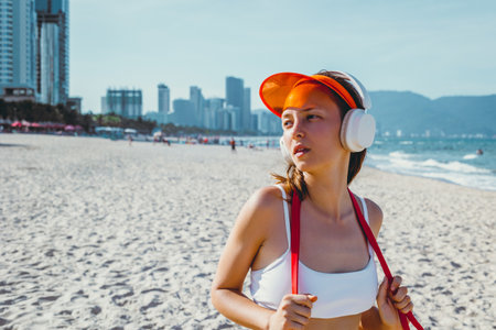 Young asian female enjoying beach workout with headphones on sunny day.の写真素材
