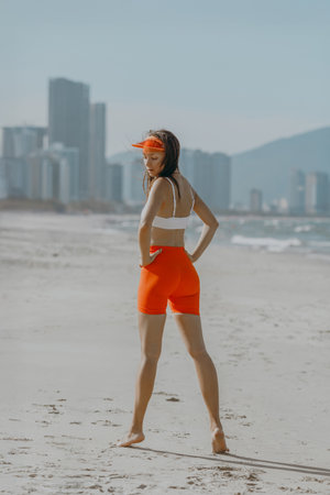 Young caucasian woman in athletic wear posing on beach with city skyline.の写真素材