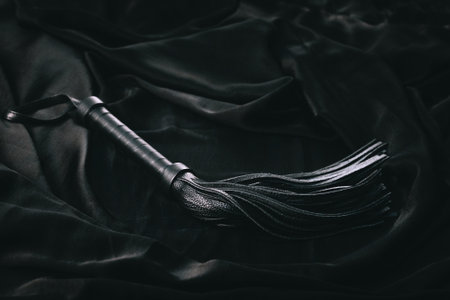 Black leather flogger on dark fabric background.の写真素材