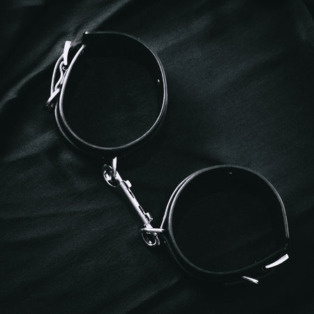 Close-up of black leather handcuffs with metal chain on dark fabric surface.の写真素材