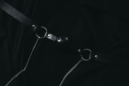 Black leather bondage gear with chains on dark fabric background.の写真素材