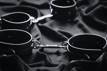 Close-up of black leather handcuffs on dark fabric background.の写真素材