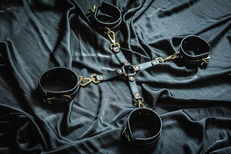 Black leather restraints on silk fabric background.の写真素材