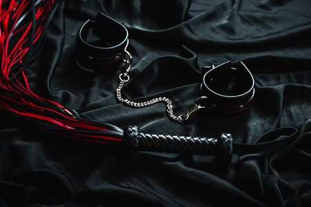 Leather handcuffs and whip on black satin fabric with red accents.の写真素材