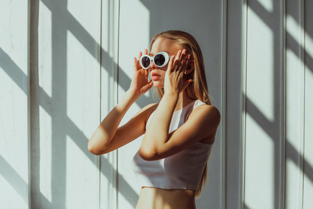 Young caucasian female adjusting sunglasses in sunlit room.の写真素材