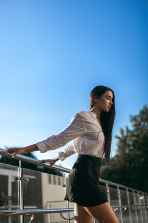 Young caucasian female in white shirt and black skirt posing outdoors by rail.の写真素材